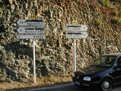 Kétnyelvű útjelző táblák Korzikán, a francia változat áthúzva – a korzikai pedig jobbára már csak nyelvemlék