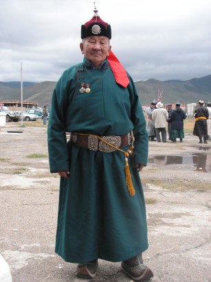 Ünnepi alkalomra hagyományos mongol viseletbe öltözött férfi. A csatos, veretes bőröv régen a férfiak viseletének fontos része volt, amit az utóbbi századokban kiszorított az egyszerű, élénk színű selyemöv, de napjainkban a hagyományok felélesztése jegyében esetenként újra megjelenik